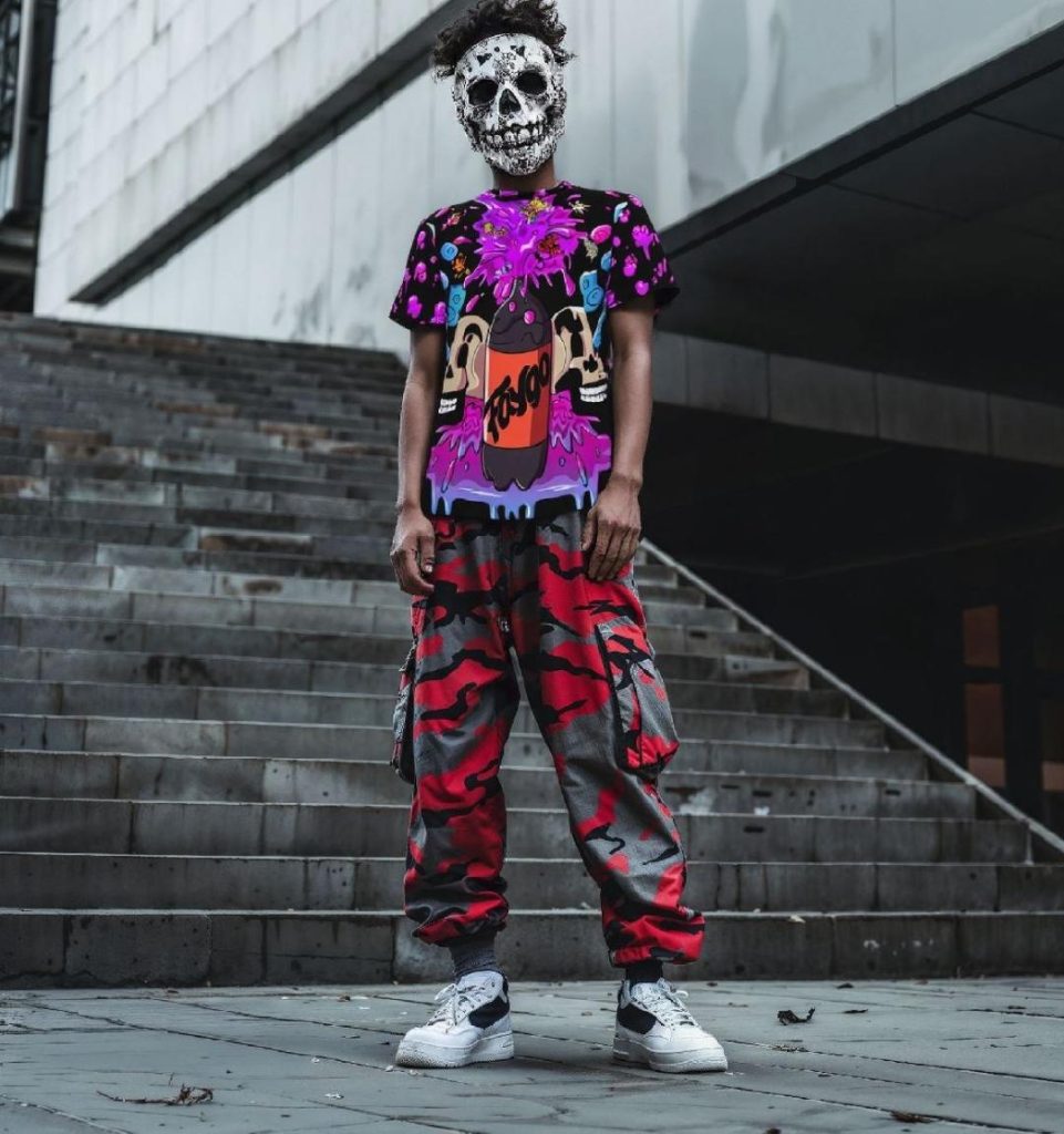 Juggalo wearing a skeleton mask and a Faygo Rain shirt, paired with red camouflage pants, standing in front of a city backdrop. The bold outfit represents streetwear style with a touch of underground culture.